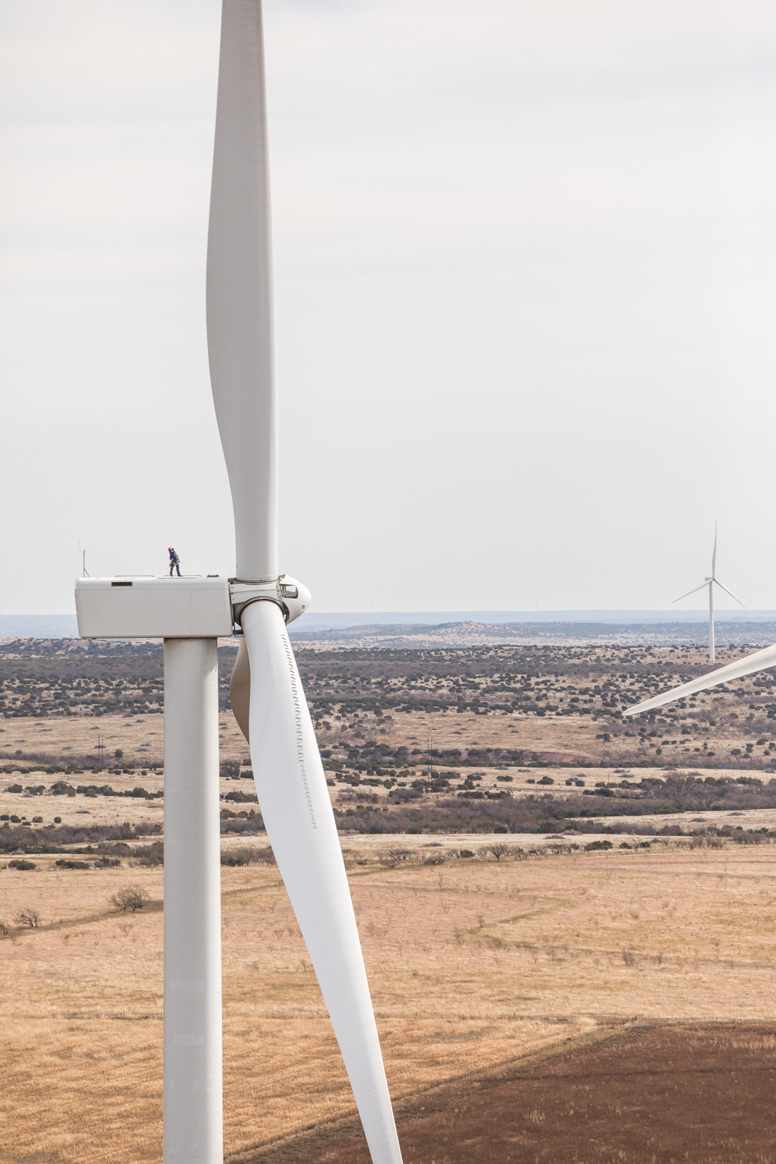 man on top of wind turbine creating clean renewable energy.