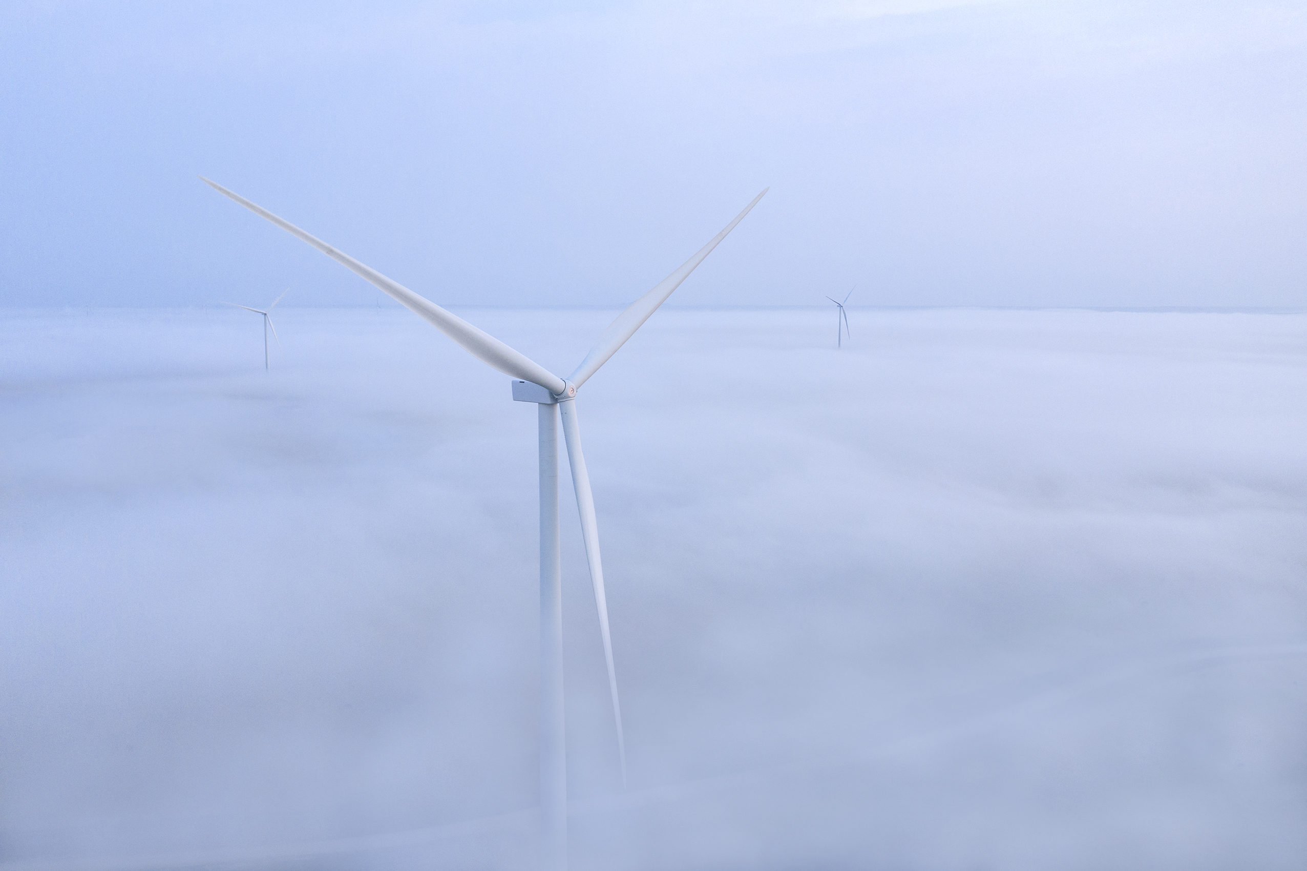 Wind turbine above fog and cloud layer on large wind farm.